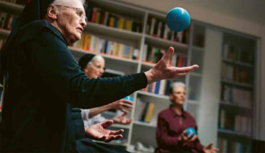 Turnstunde Schwestern - © CONCORDIA Kundenmagazin «CARE» Betagte Klosterfrau, mit der Hand einen Ball aufwerfend